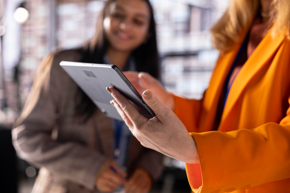 Duas profissionais analisam informações em um tablet em ambiente corporativo ou logístico.
