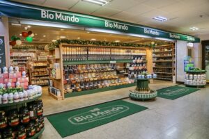 Fachada interna de loja Bio Mundo com prateleiras de produtos naturais, suplementos e alimentos saudáveis organizados.