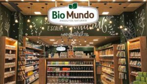 Interior de uma loja da Bio Mundo, com prateleiras organizadas cheias de produtos naturais, suplementos e alimentos saudáveis, iluminação quente e decoração em tons de verde com ilustrações de plantas.